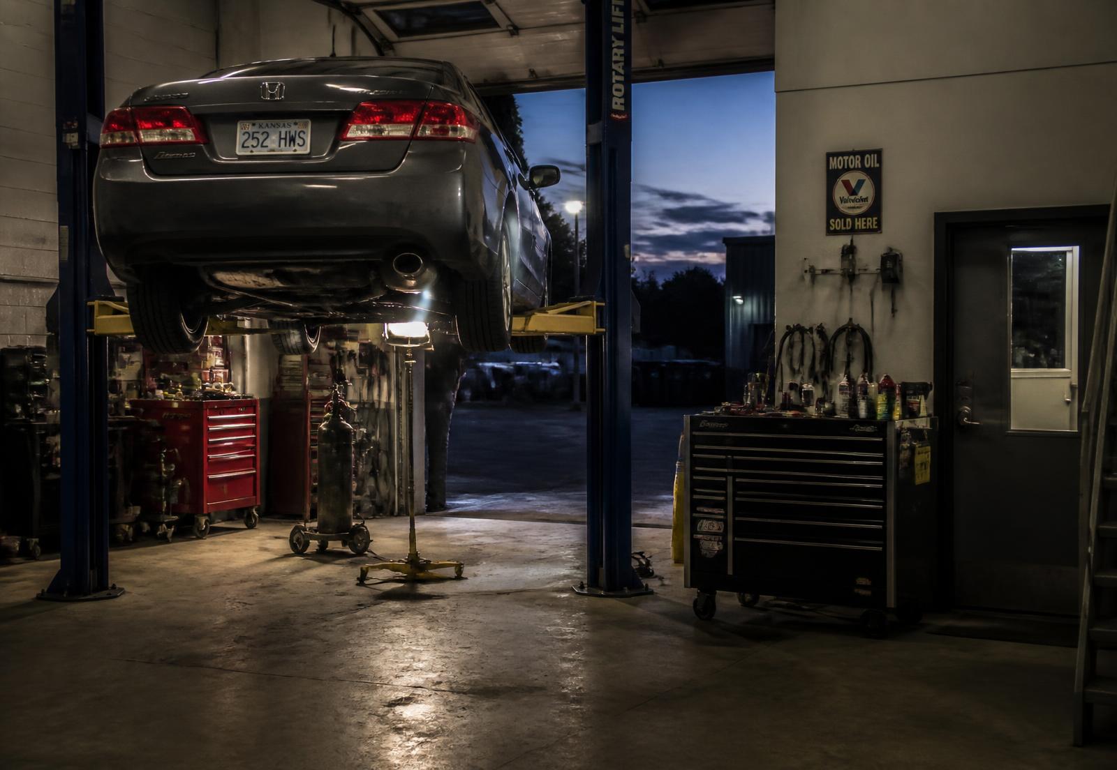 Car raised on a two-post lift inside Kyle's Elite Auto Services at dusk